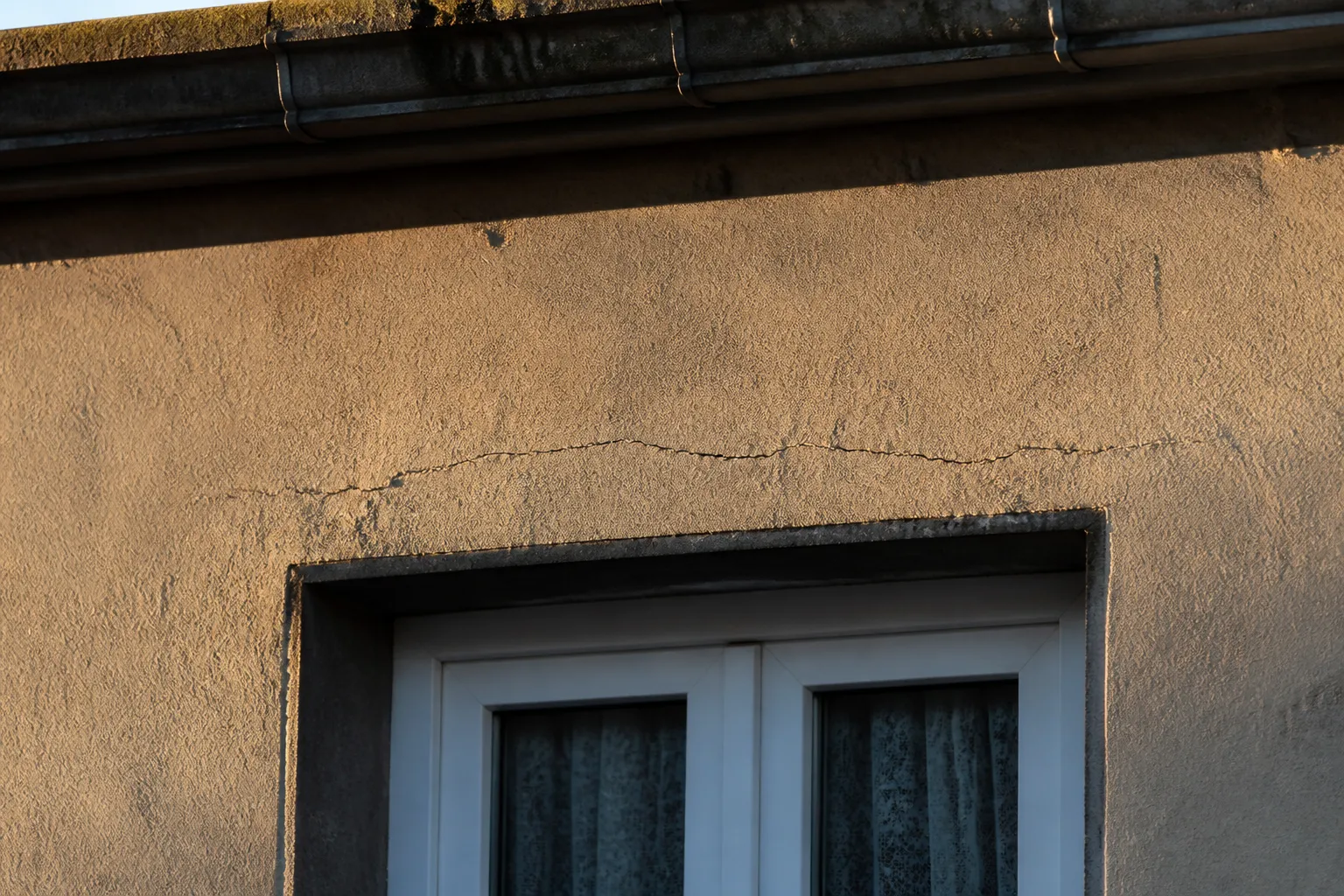Façade enduite de maison ouvrière avec fissure fine au-dessus d’une fenêtre