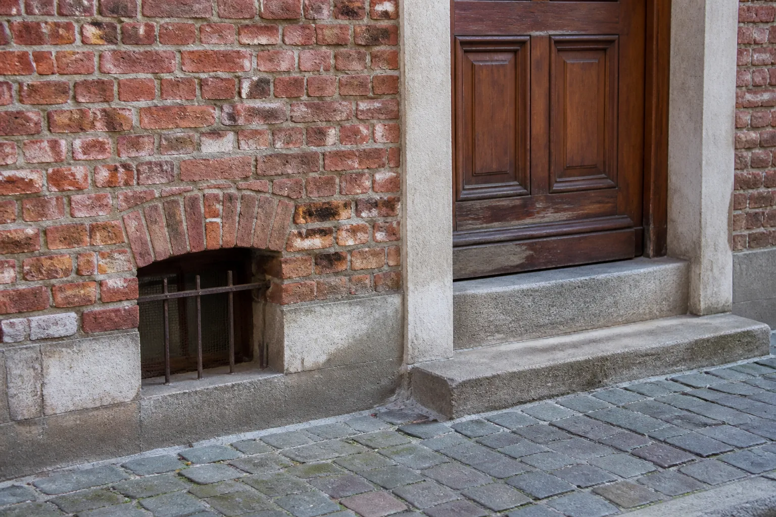 Seuil de porte et soupirail d’une maison vus depuis la rue