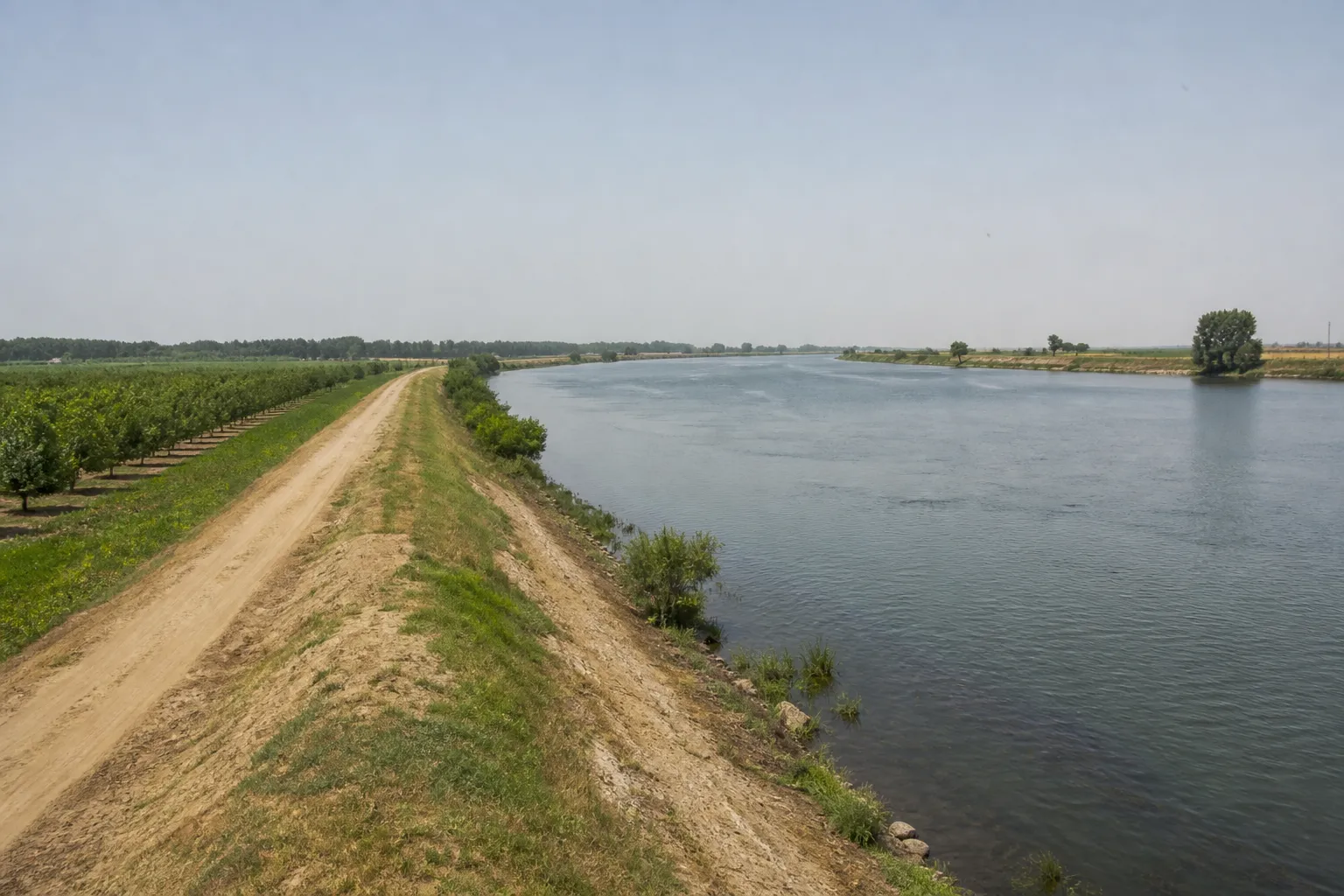 Digue en terre longeant une rivière large en plaine agricole