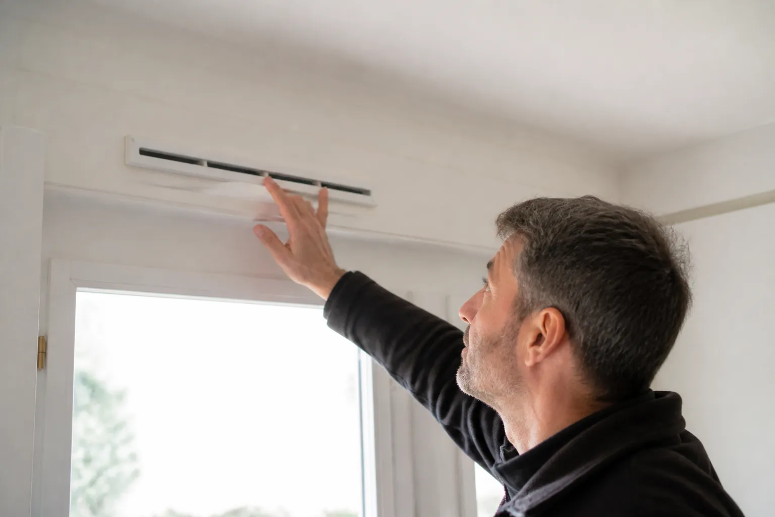 Expert en bâtiment observant une entrée d’air au-dessus d’une fenêtre