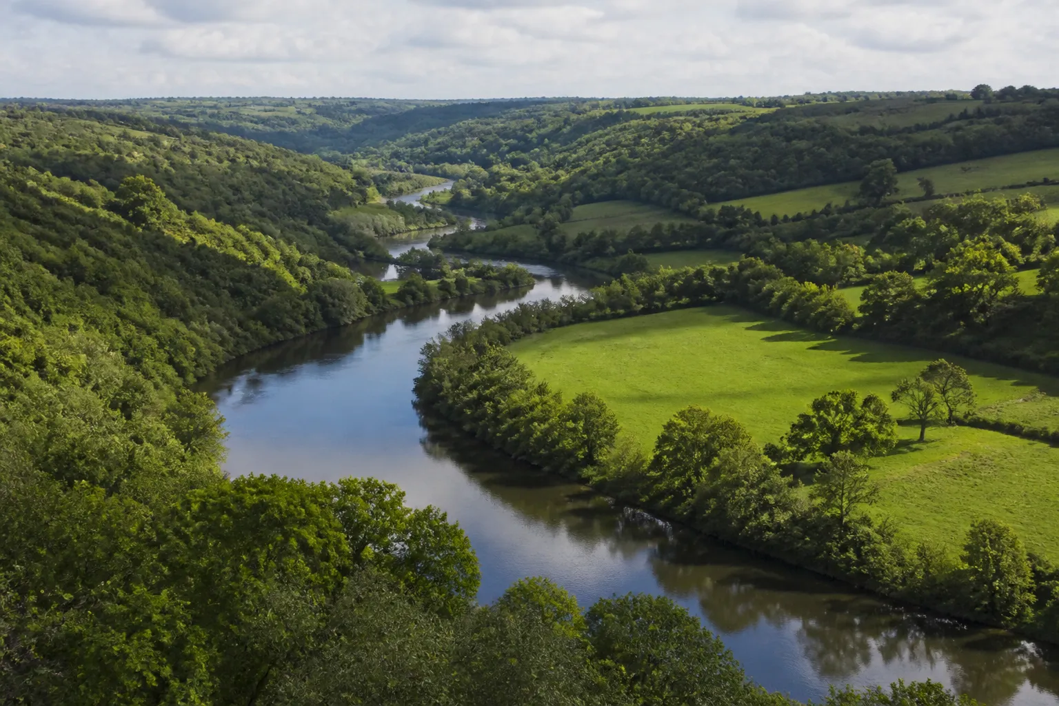 Rivière sinueuse bordée d’arbres dans une vallée bocagère