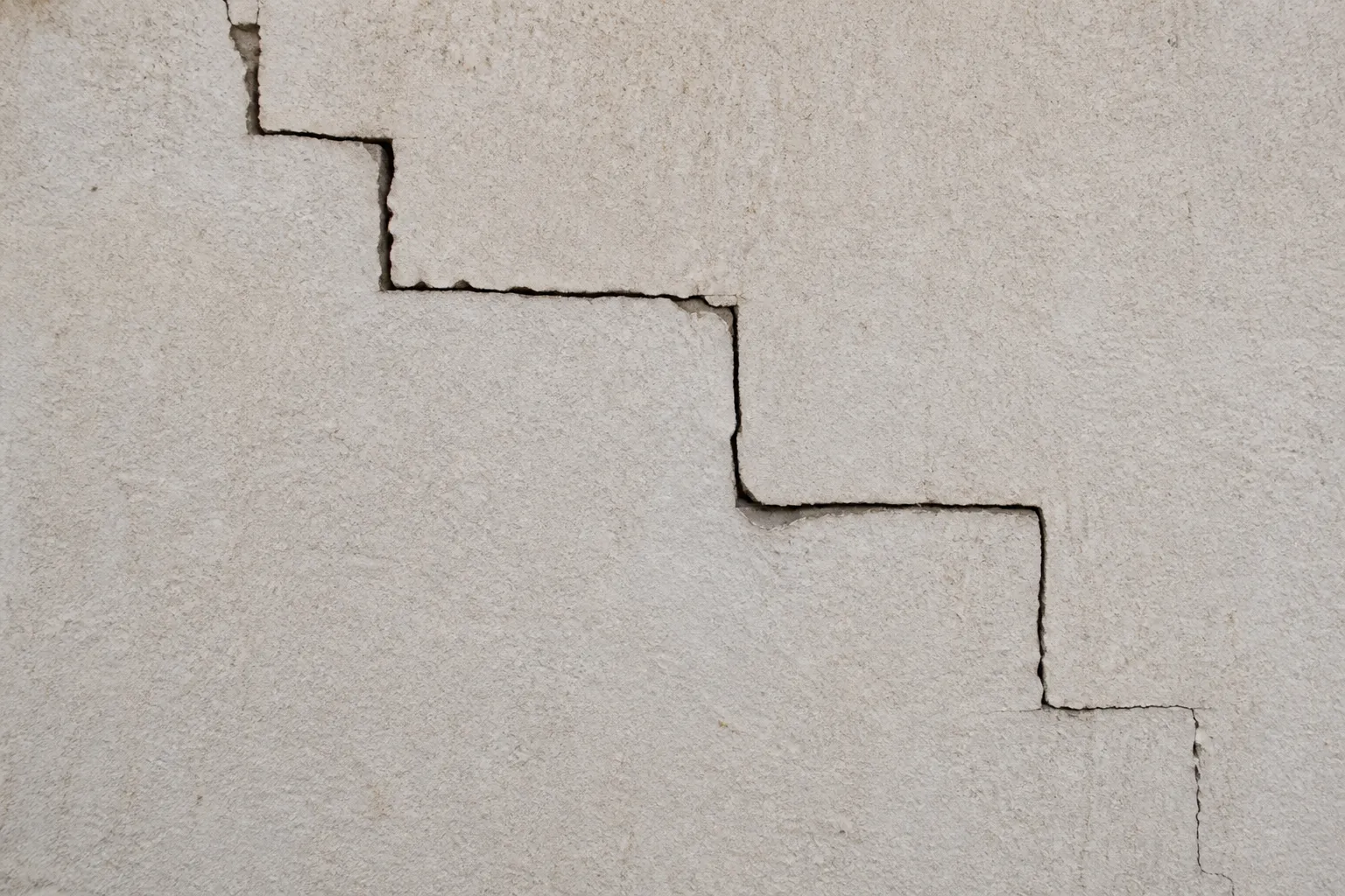 Fissure en escalier sur un mur de façade en parpaing enduit