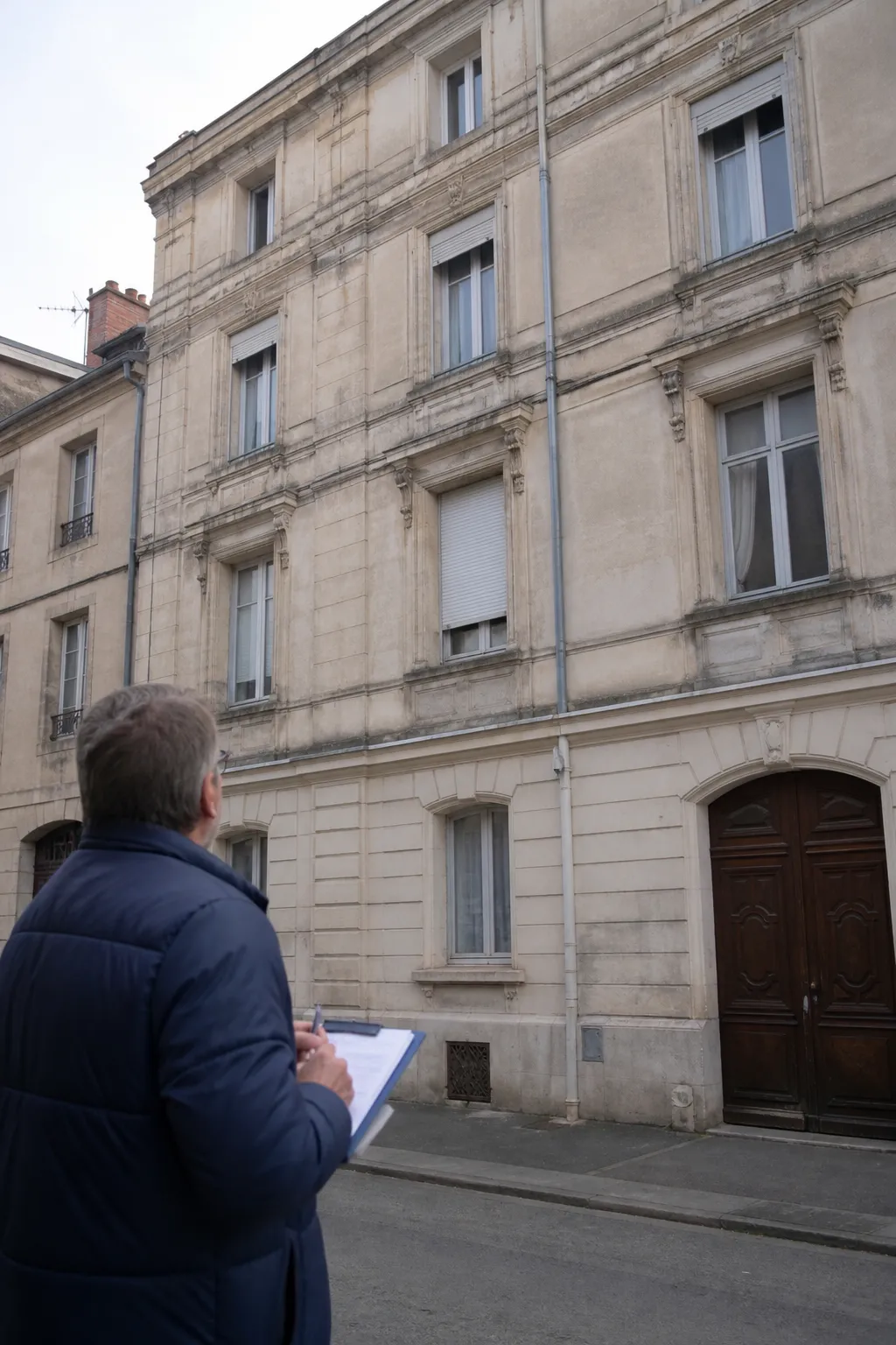 Expert en bâtiment observant un immeuble ancien avant un achat à Belfort