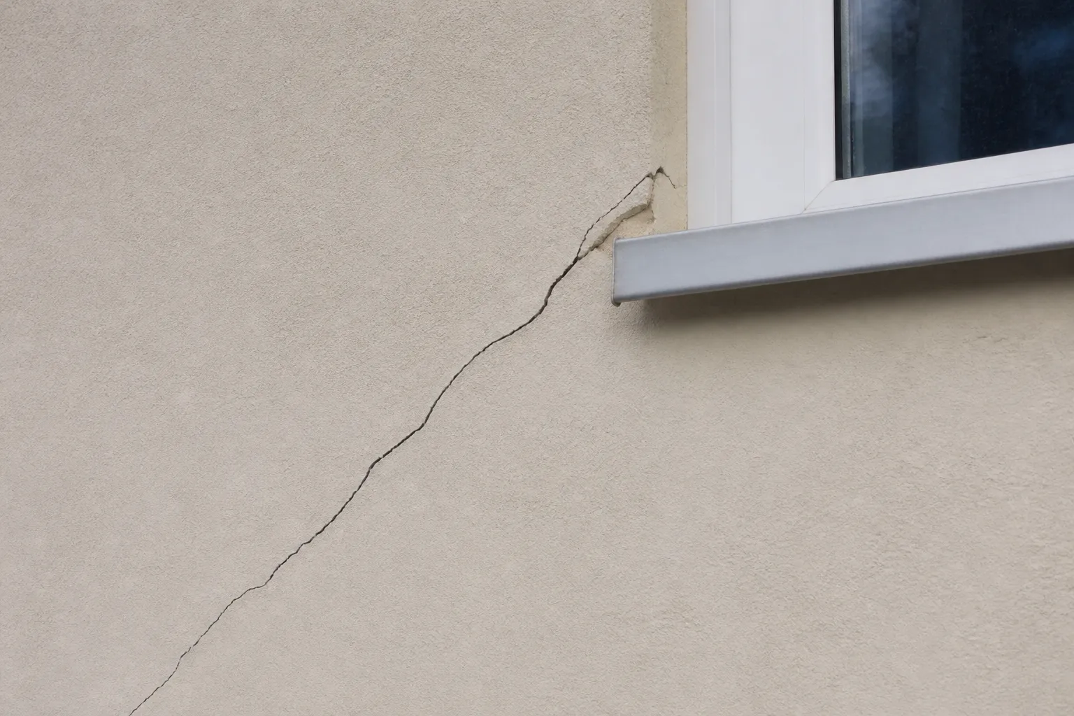 Fissure oblique partant de l’angle d’une fenêtre sur une façade enduite