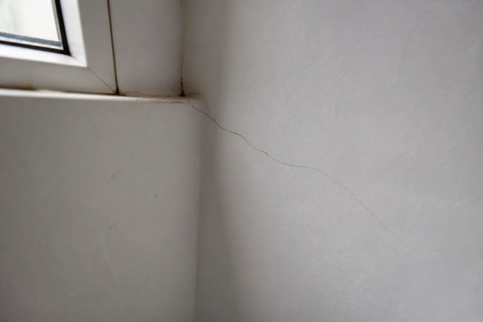 Fissure oblique sur un mur intérieur partant d'un angle de fenêtre