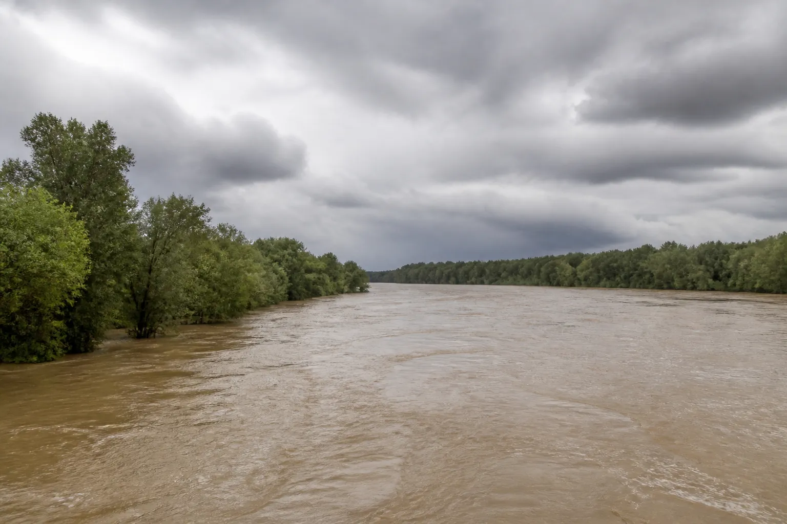 Fleuve large en hautes eaux sous un ciel gris