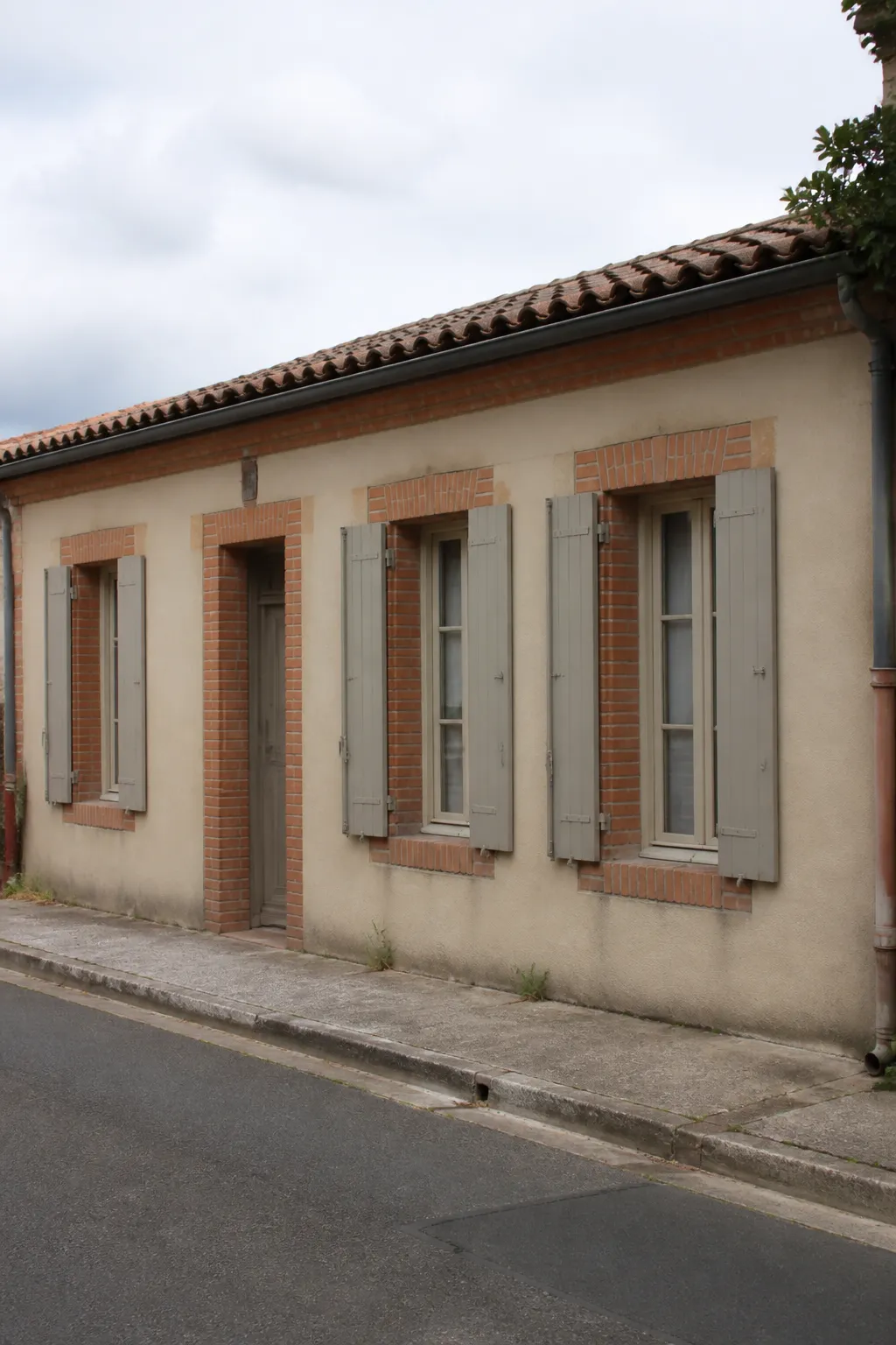 Façade d’une maison de faubourg en rez-de-chaussée avec encadrements de briques et enduit
