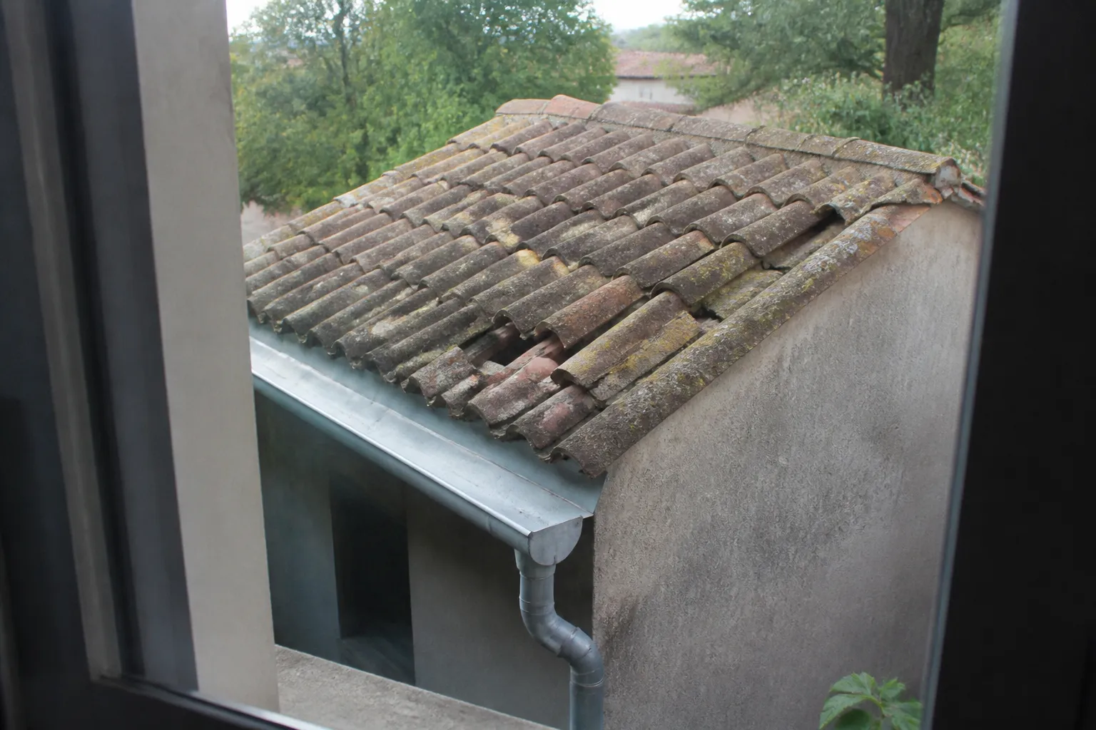 Toiture en tuiles avec quelques tuiles cassées et gouttière vue depuis une fenêtre