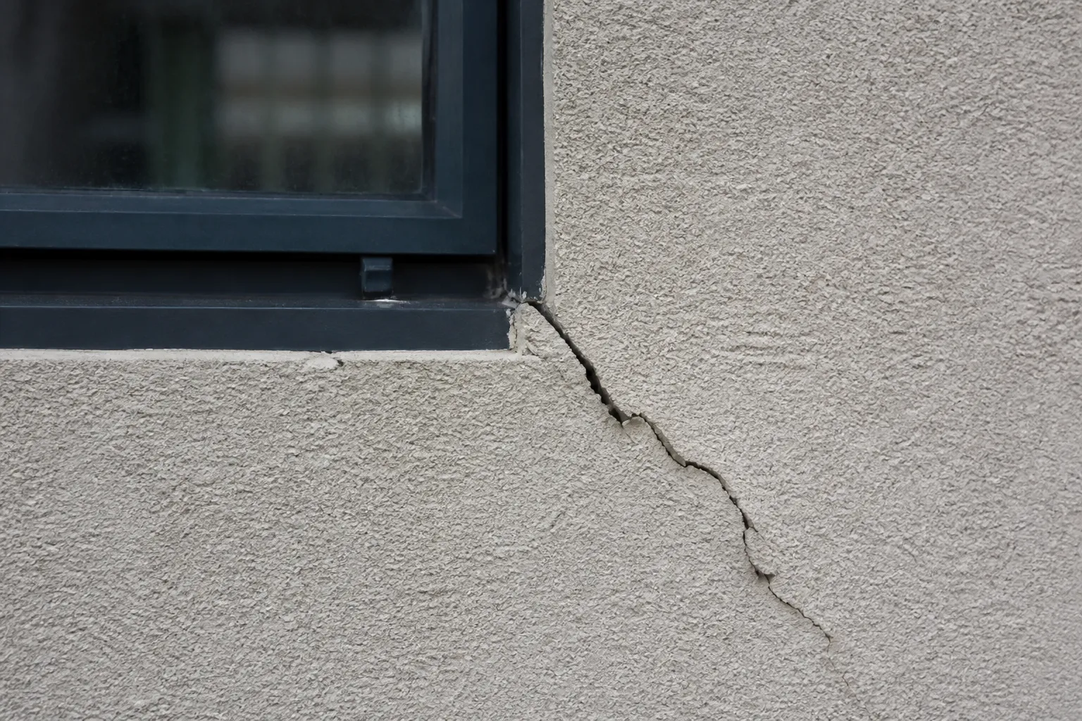 Fissure oblique à l’angle d’une fenêtre sur une façade crépie