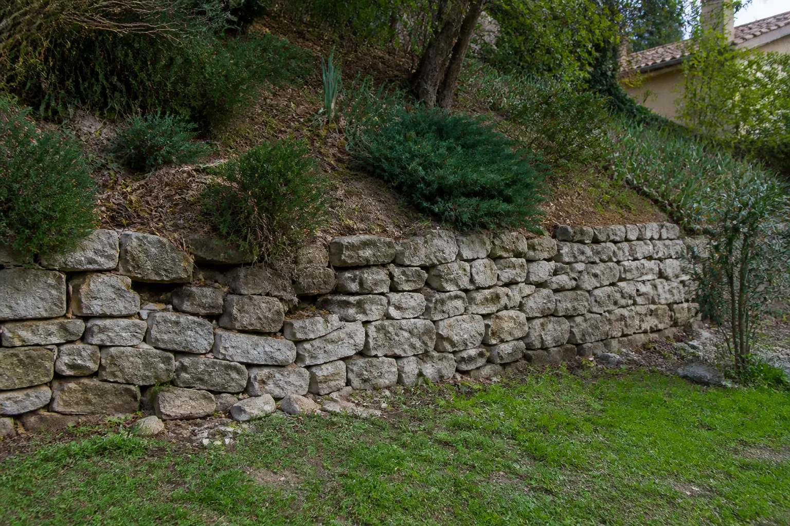 Mur de soutènement en pierre au pied d’un talus derrière une maison