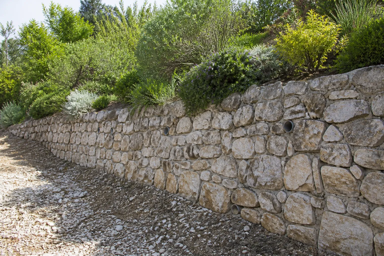 Mur de soutènement en pierre avec barbacanes sous un jardin en pente