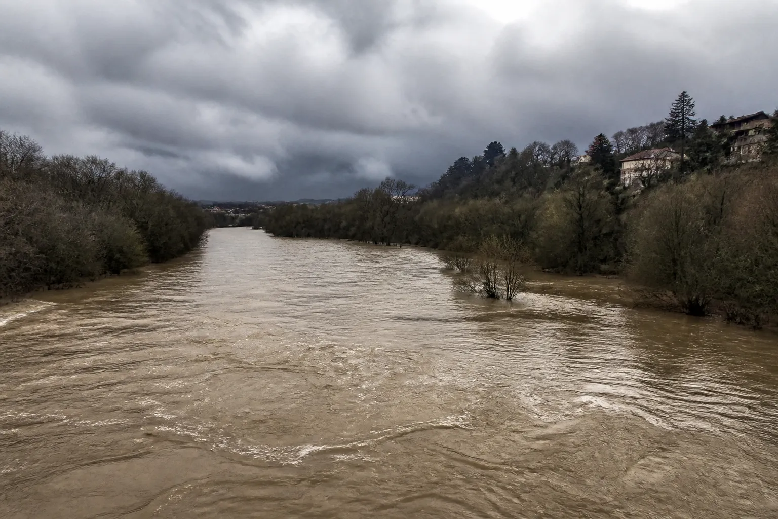 Rivière en crue boueuse sous un ciel d’orage