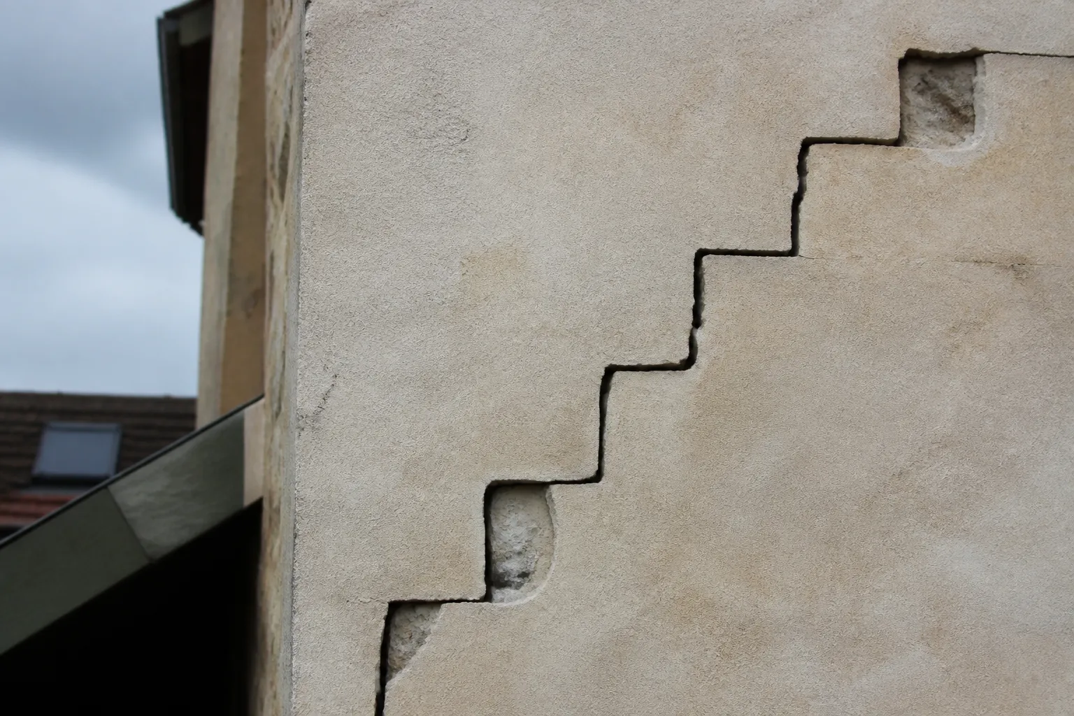 Fissure en escalier sur un mur extérieur en moellons enduits