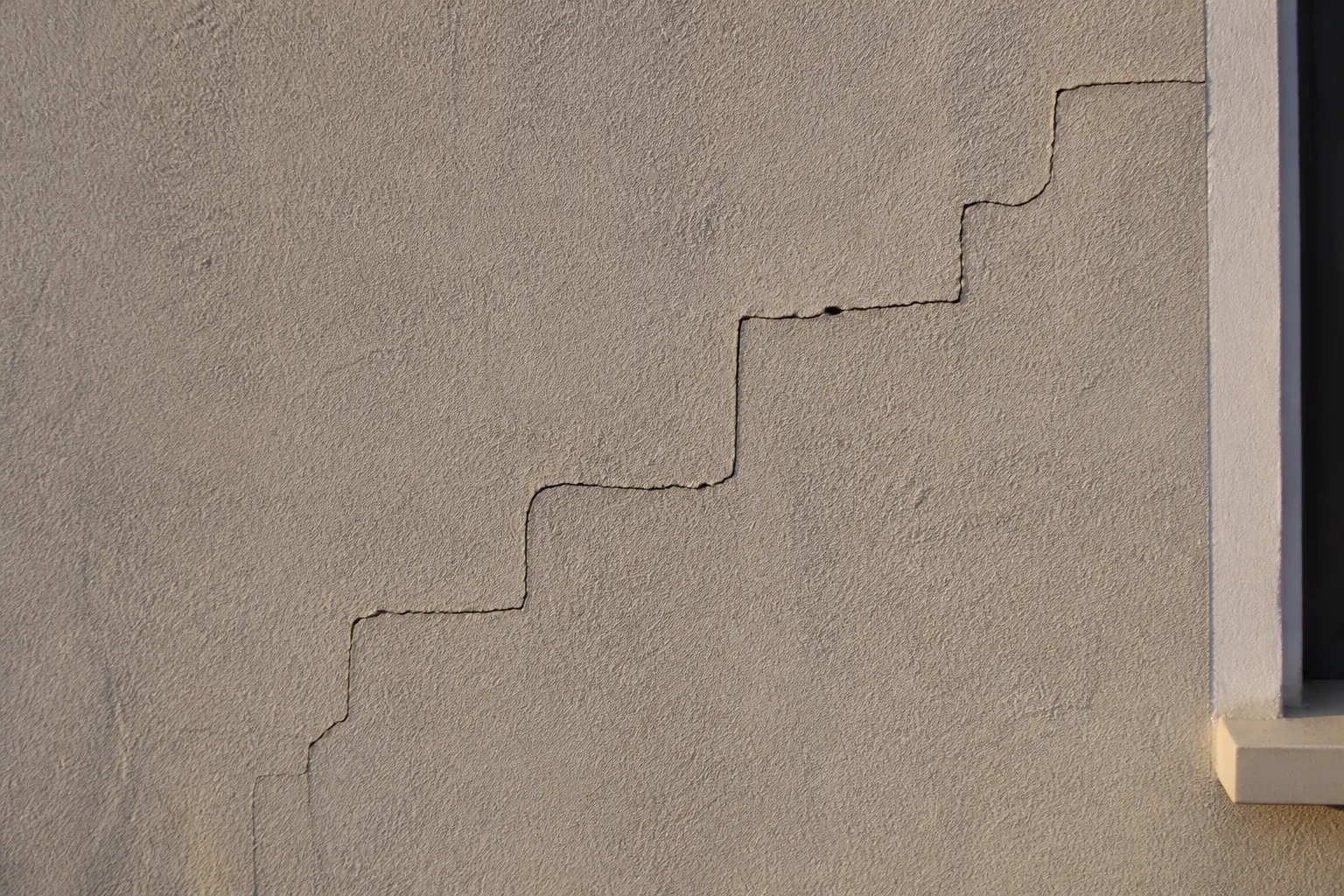 Fissure en escalier sur un mur de façade enduit