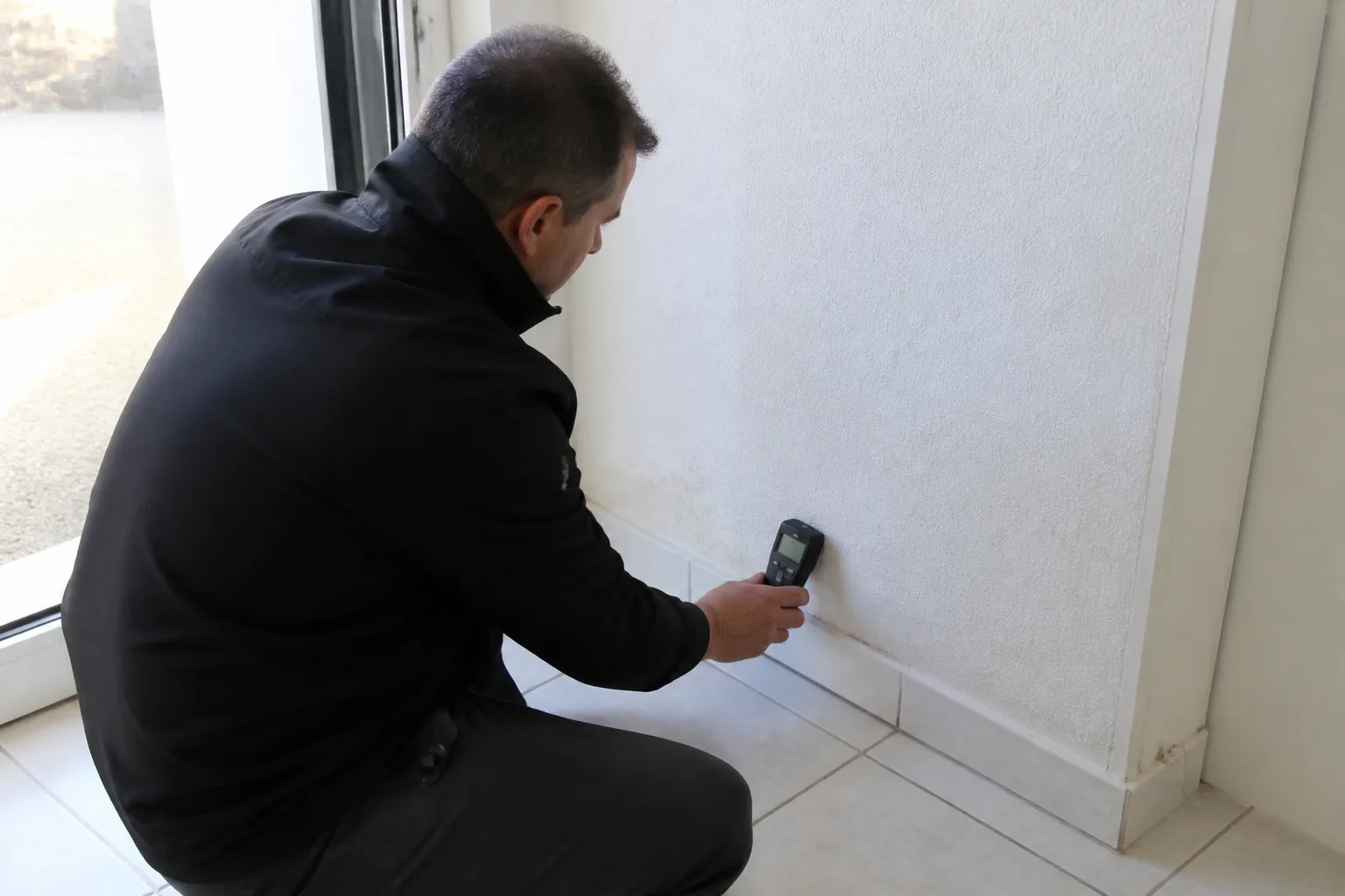 Expert en bâtiment mesurant l’humidité au pied d’un mur