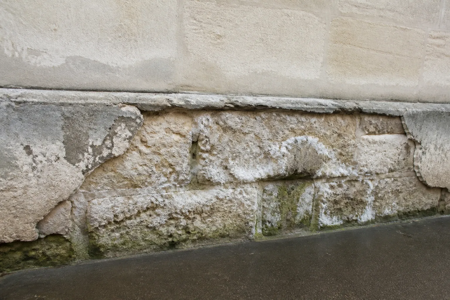 Pied de mur en pierre calcaire avec traces d’humidité et enduit dégradé