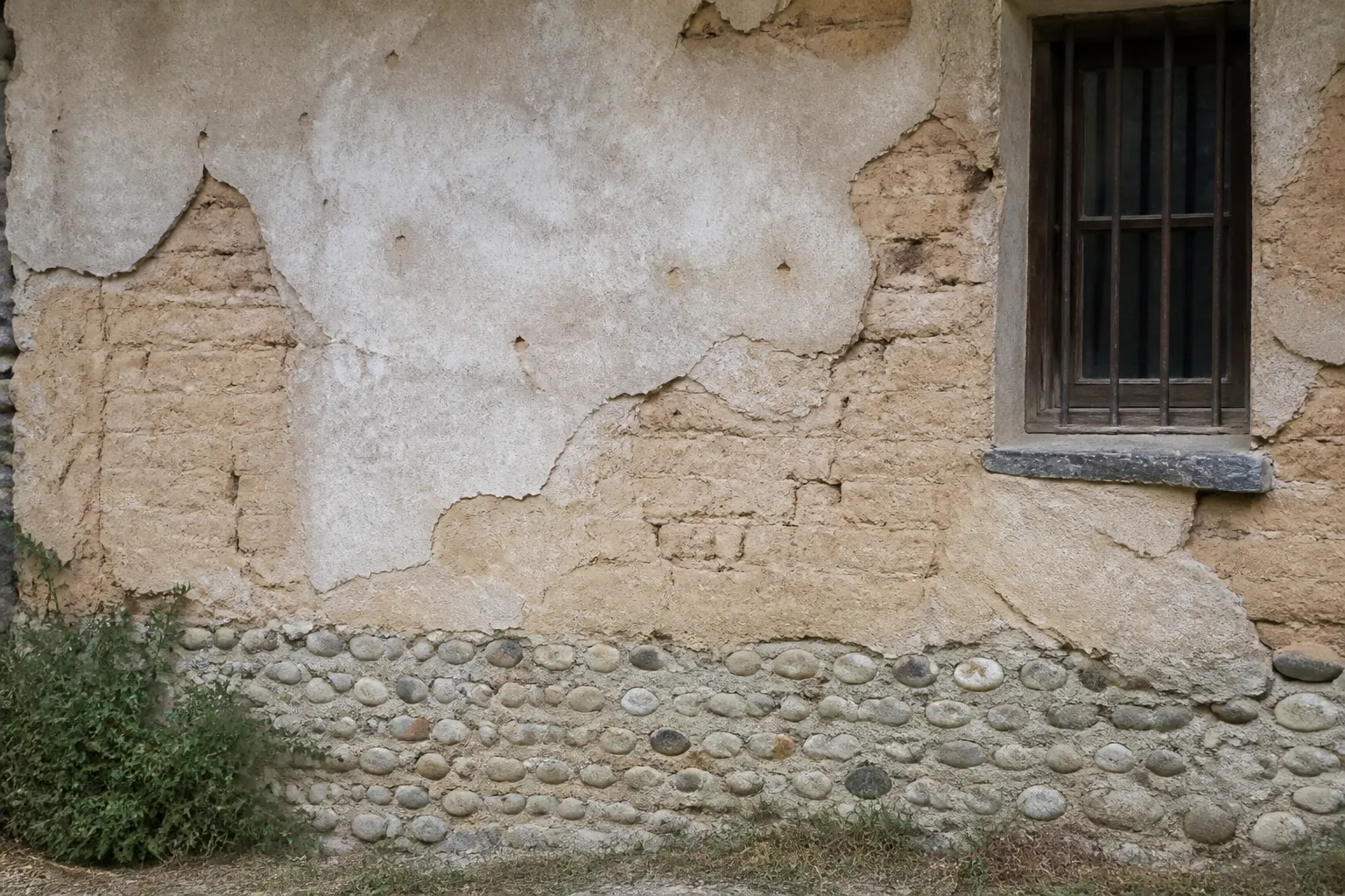 Mur ancien en terre crue avec enduit à la chaux et soubassement en galets