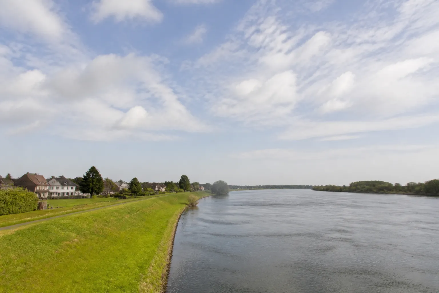 Grande rivière en plaine avec digue enherbée et maisons en retrait