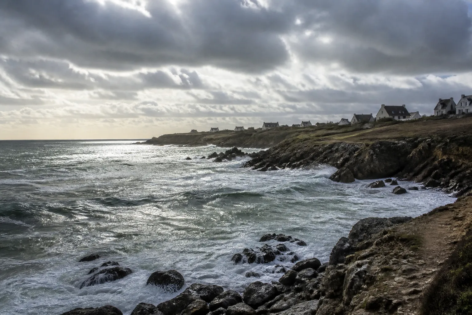 Côte rocheuse et maisons en retrait sous un ciel de tempête