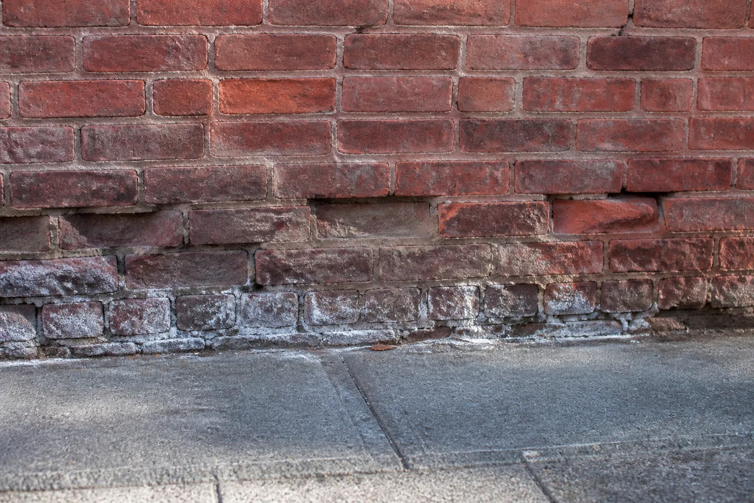 Pied de façade en brique avec joints à reprendre et trace d'humidité