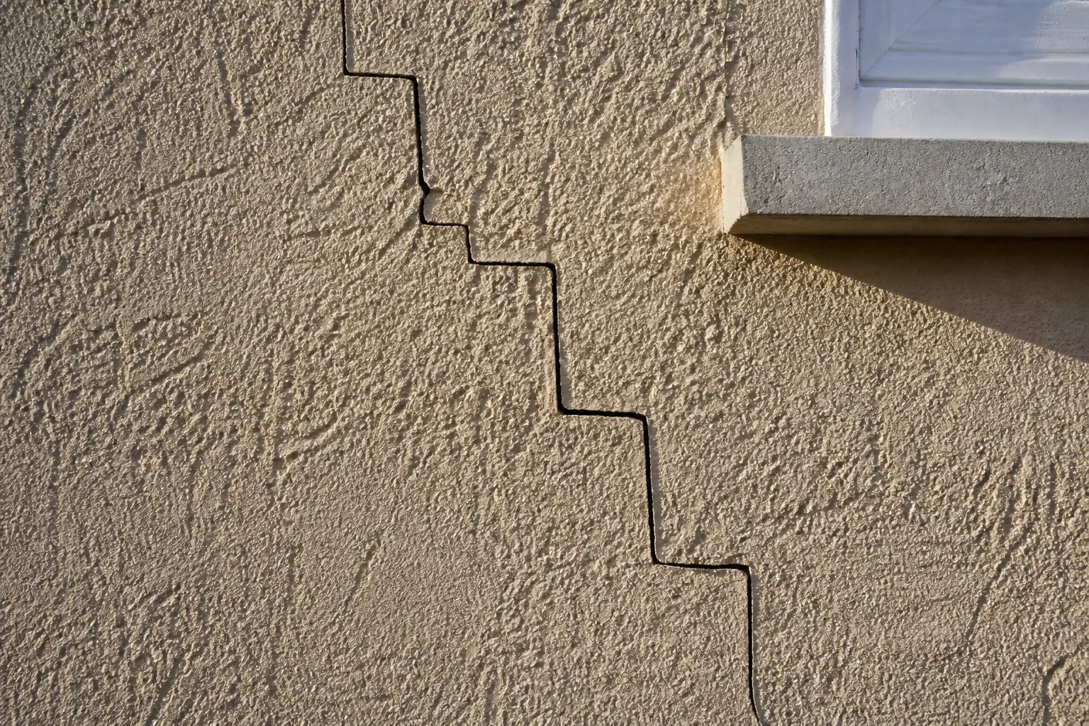 Fissure en escalier sur un mur de façade enduit