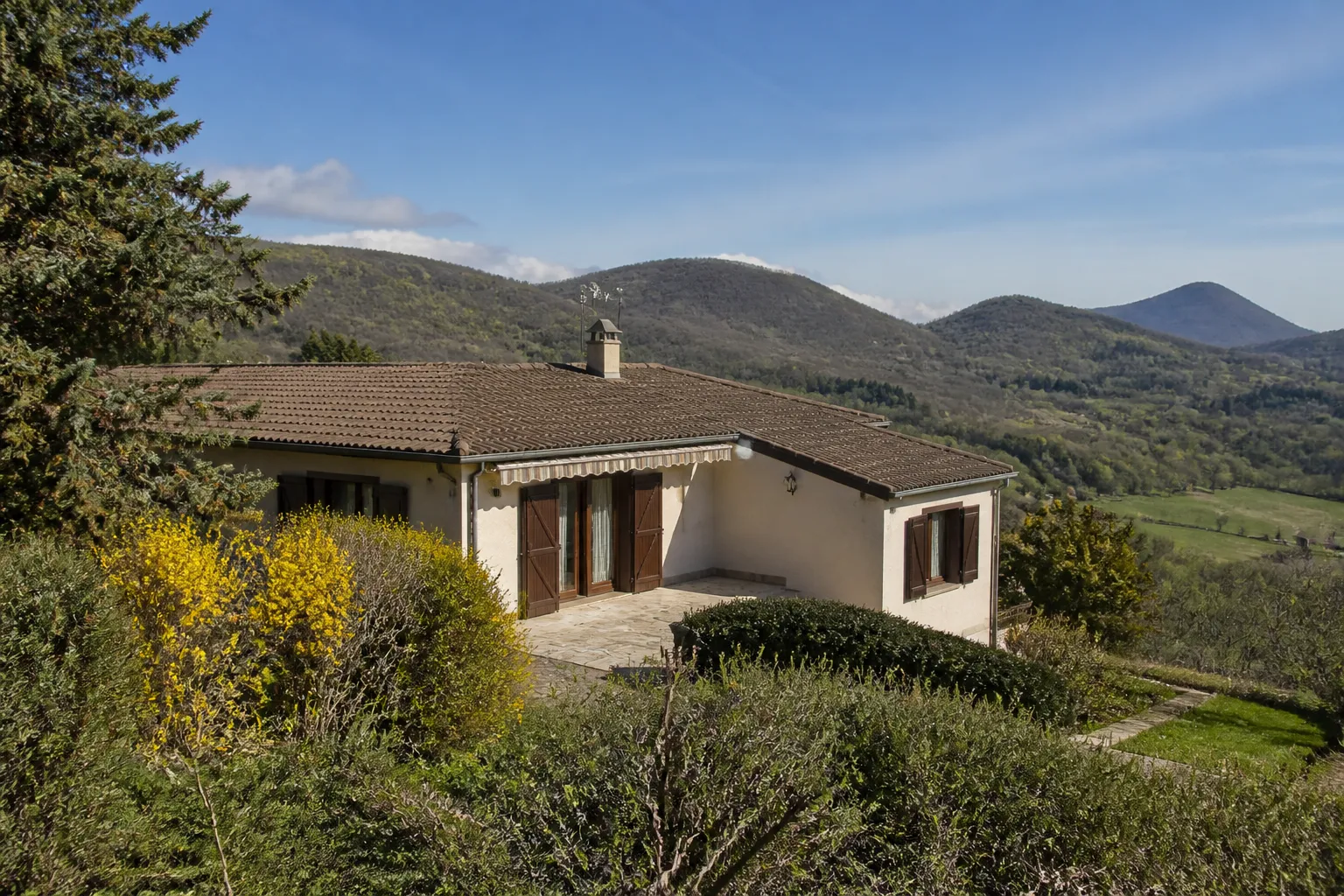Maison individuelle sur un coteau avec des reliefs volcaniques boisés à l’horizon