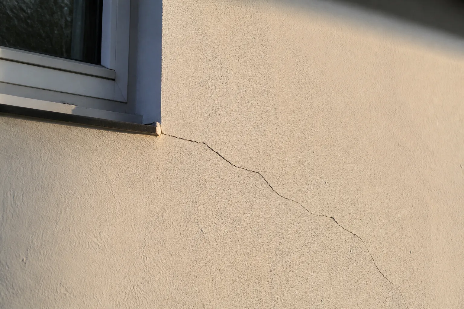 Façade de maison présentant une fissure oblique au-dessus d’une fenêtre