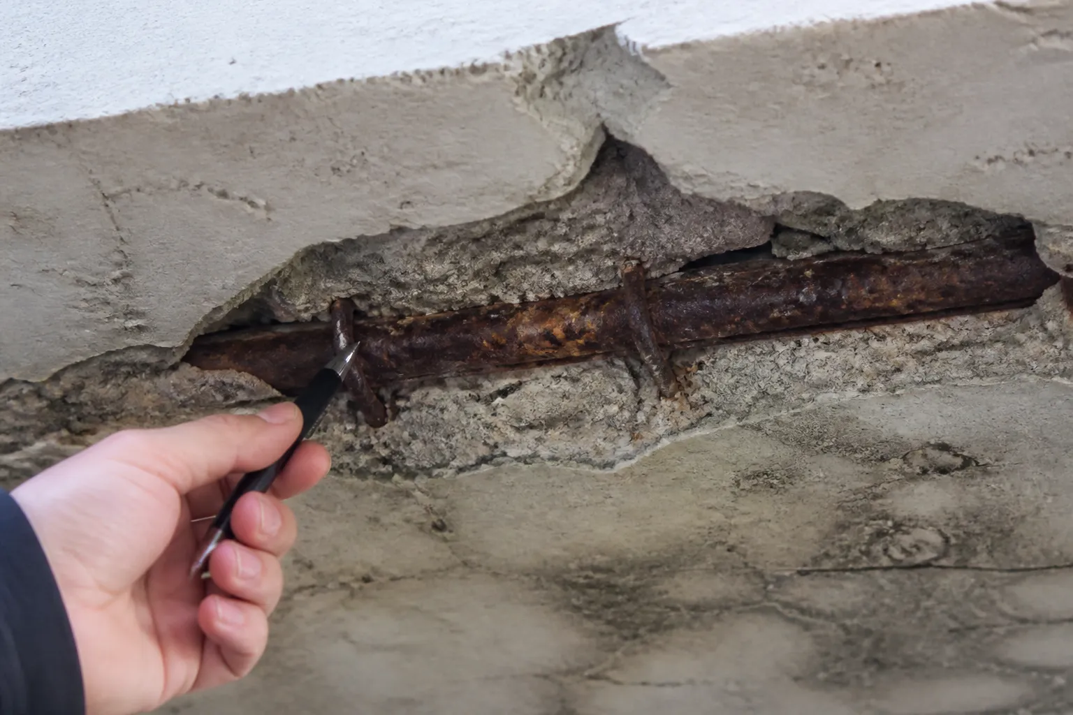 Éclat de béton laissant apparaître une armature corrodée sous un balcon