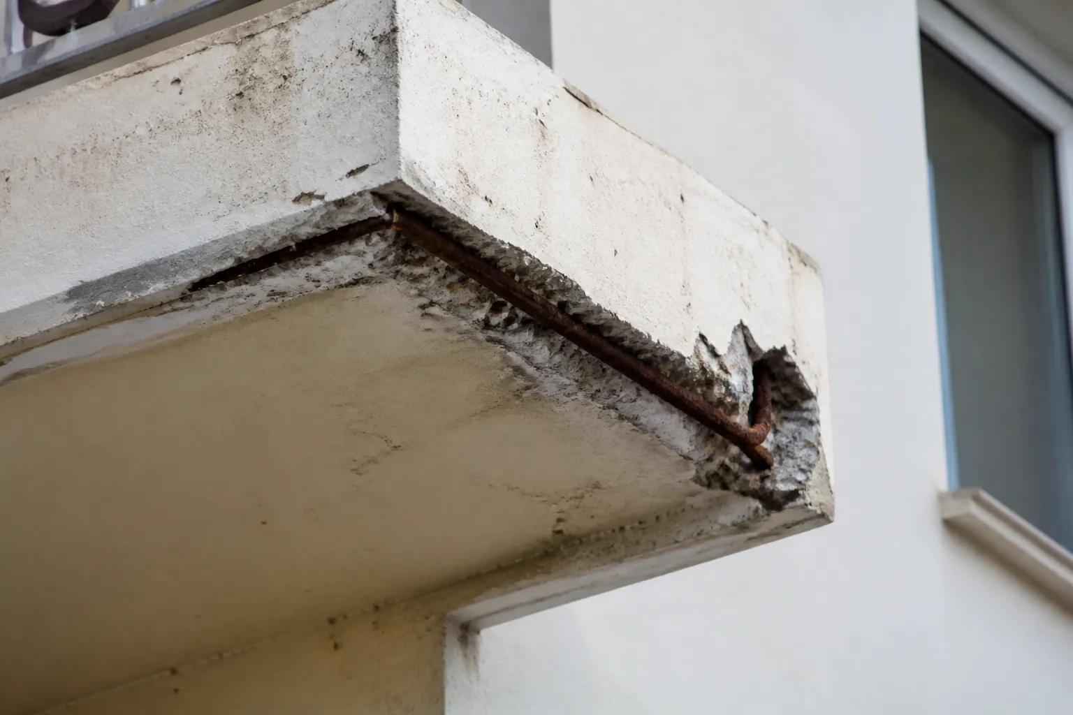 Balcon en béton avec éclat laissant voir une armature rouillée