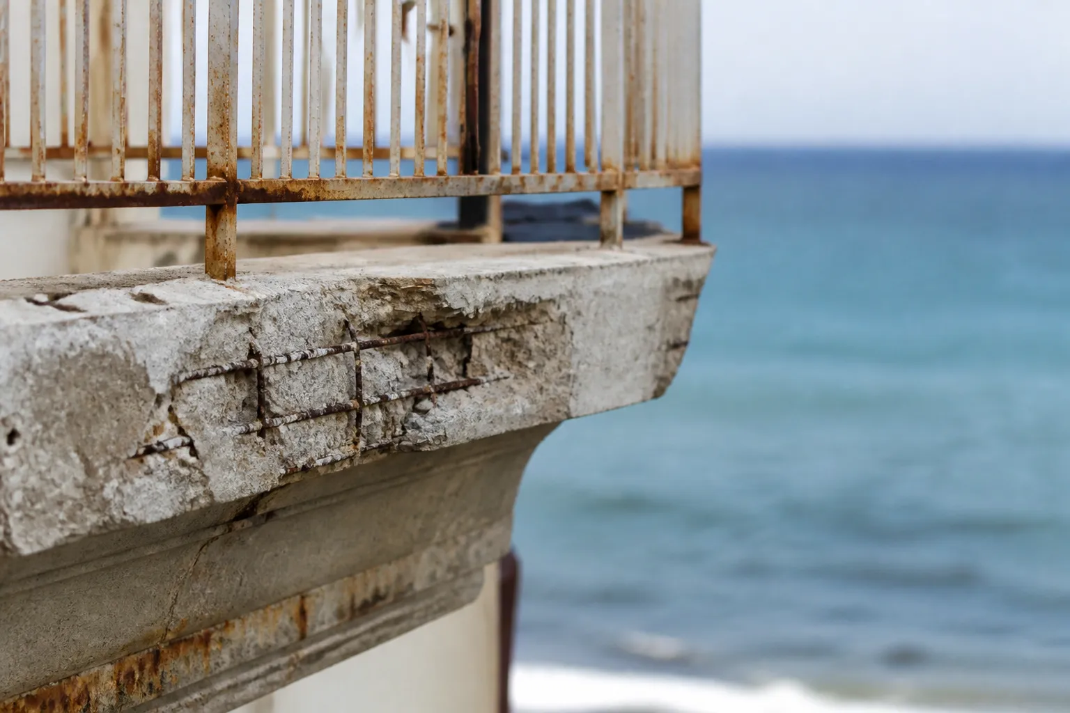 Garde-corps métallique corrodé et béton éclaté sur un balcon en bord de mer