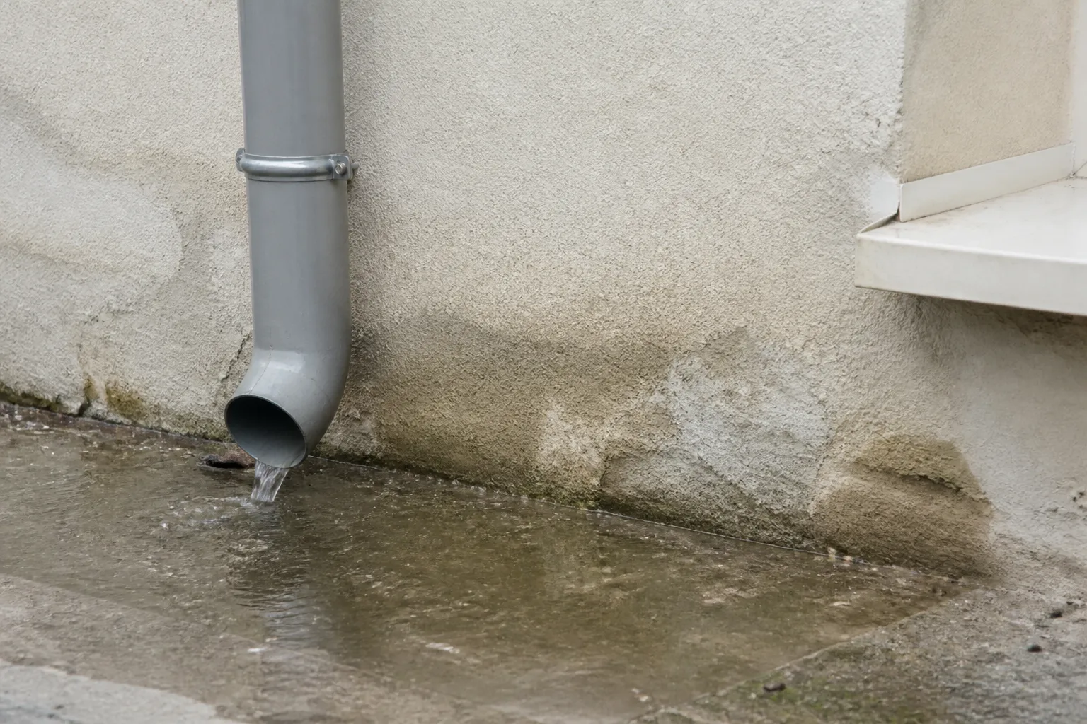 Descente d’eaux pluviales rejetant l’eau au pied d’un mur