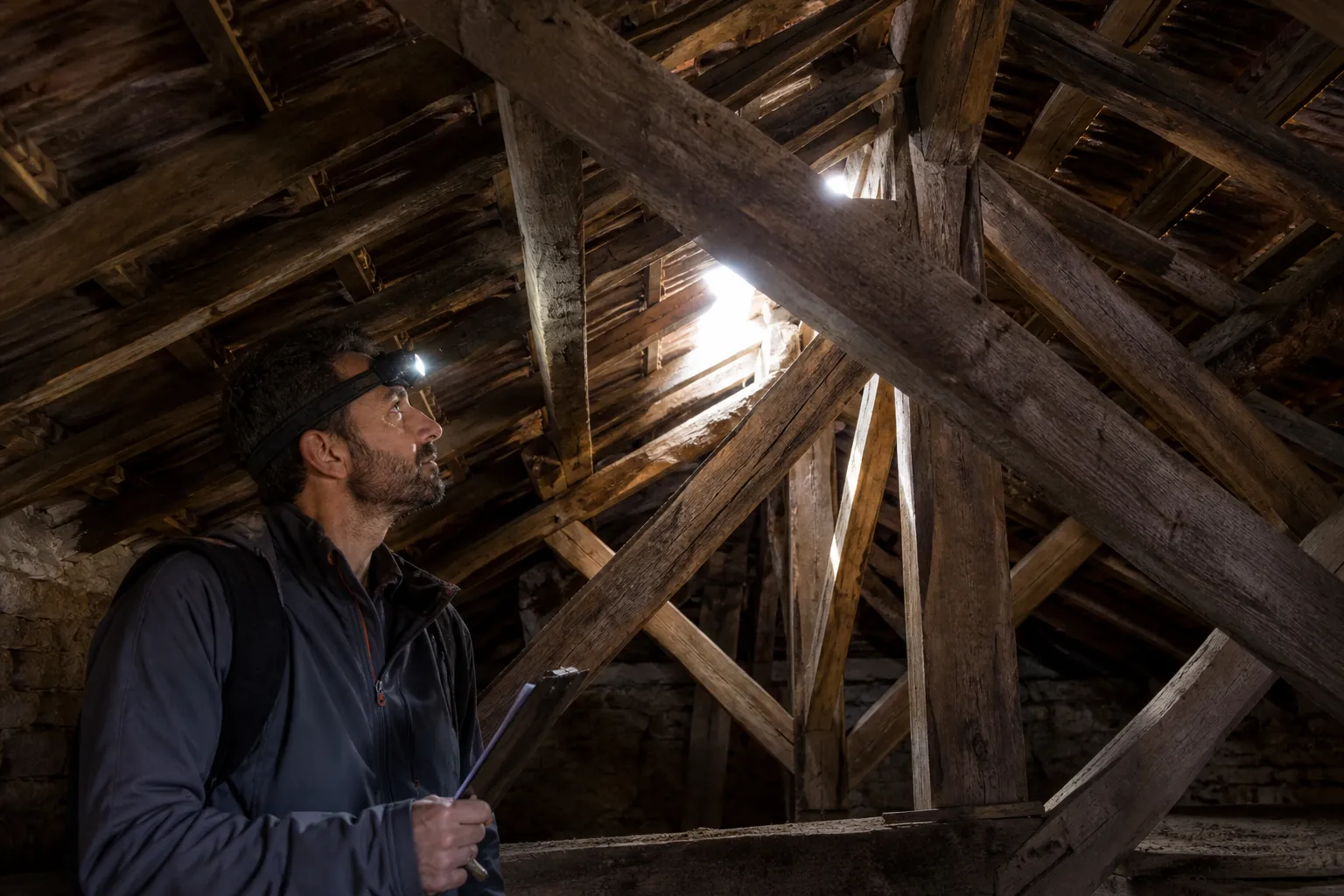 Expert en bâtiment inspectant une charpente ancienne dans des combles avec une lampe