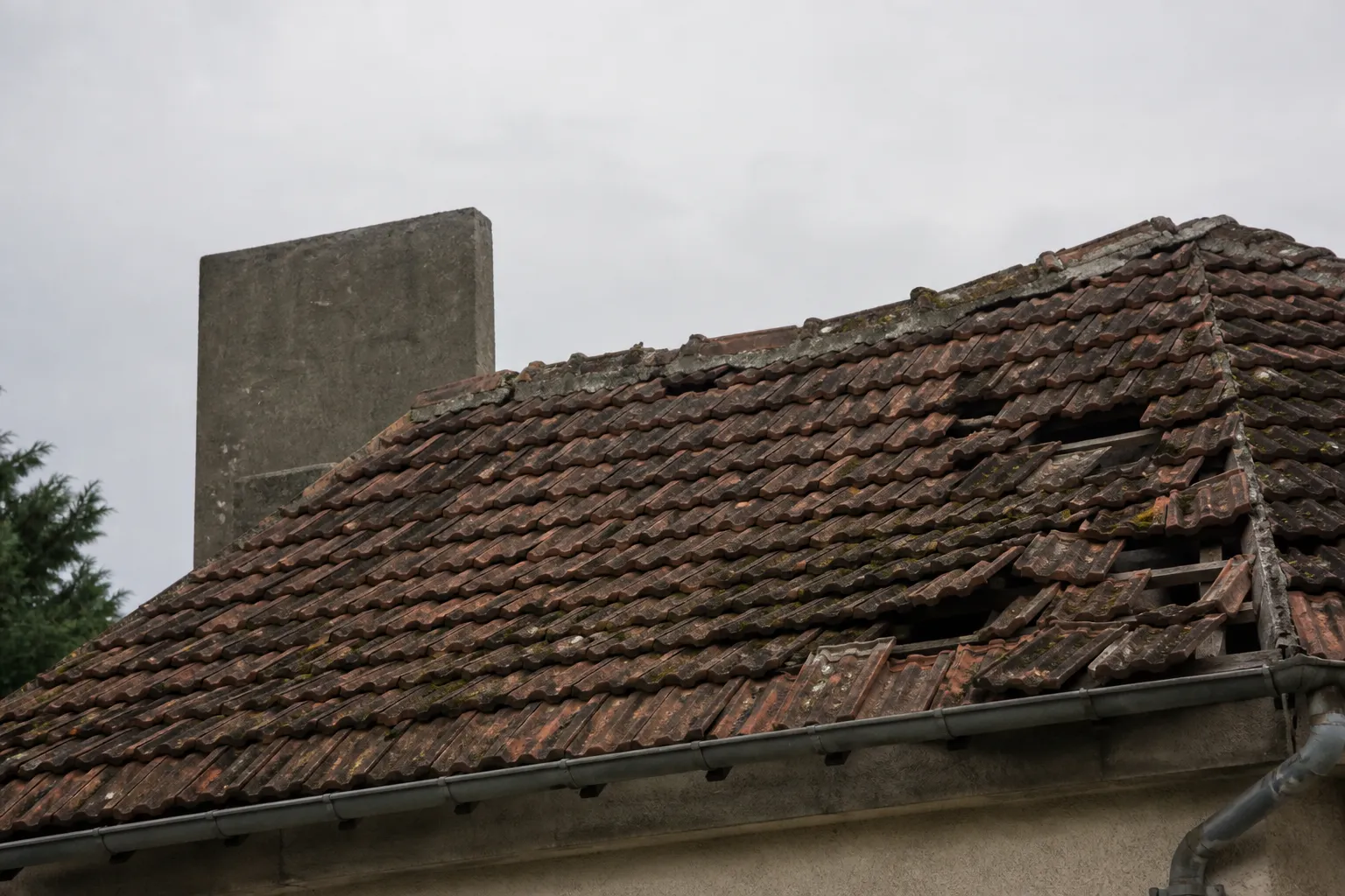 Toiture en tuiles avec tuiles glissées et mousse sur une maison